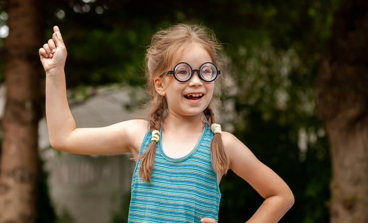 Kleines Mädchen mit Brille zeigt mit Finger nach oben.