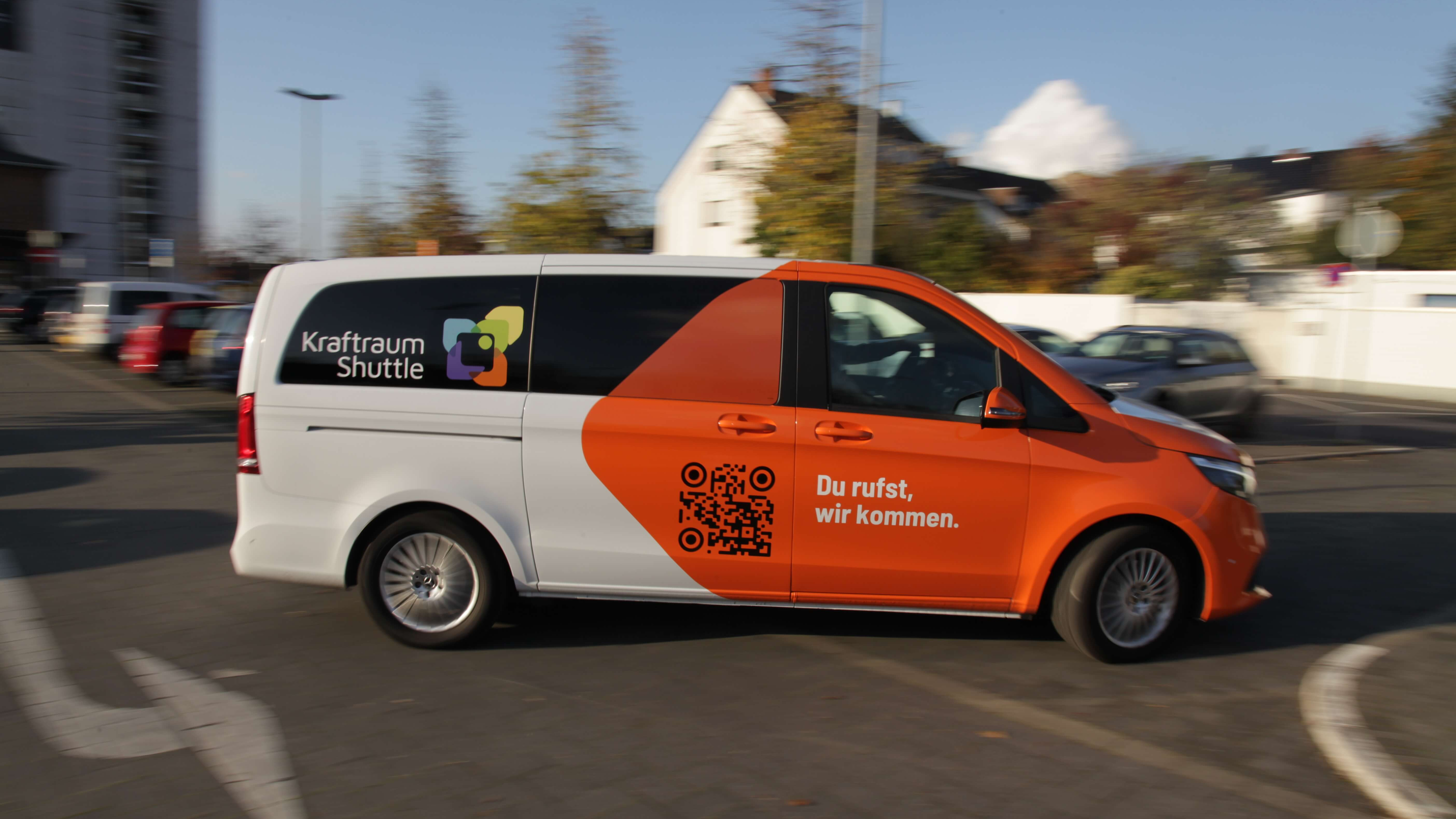 Seitliche Ansicht des fahrenden Kraftraum-Shuttles, mit Logo, Slogan und QR-Code