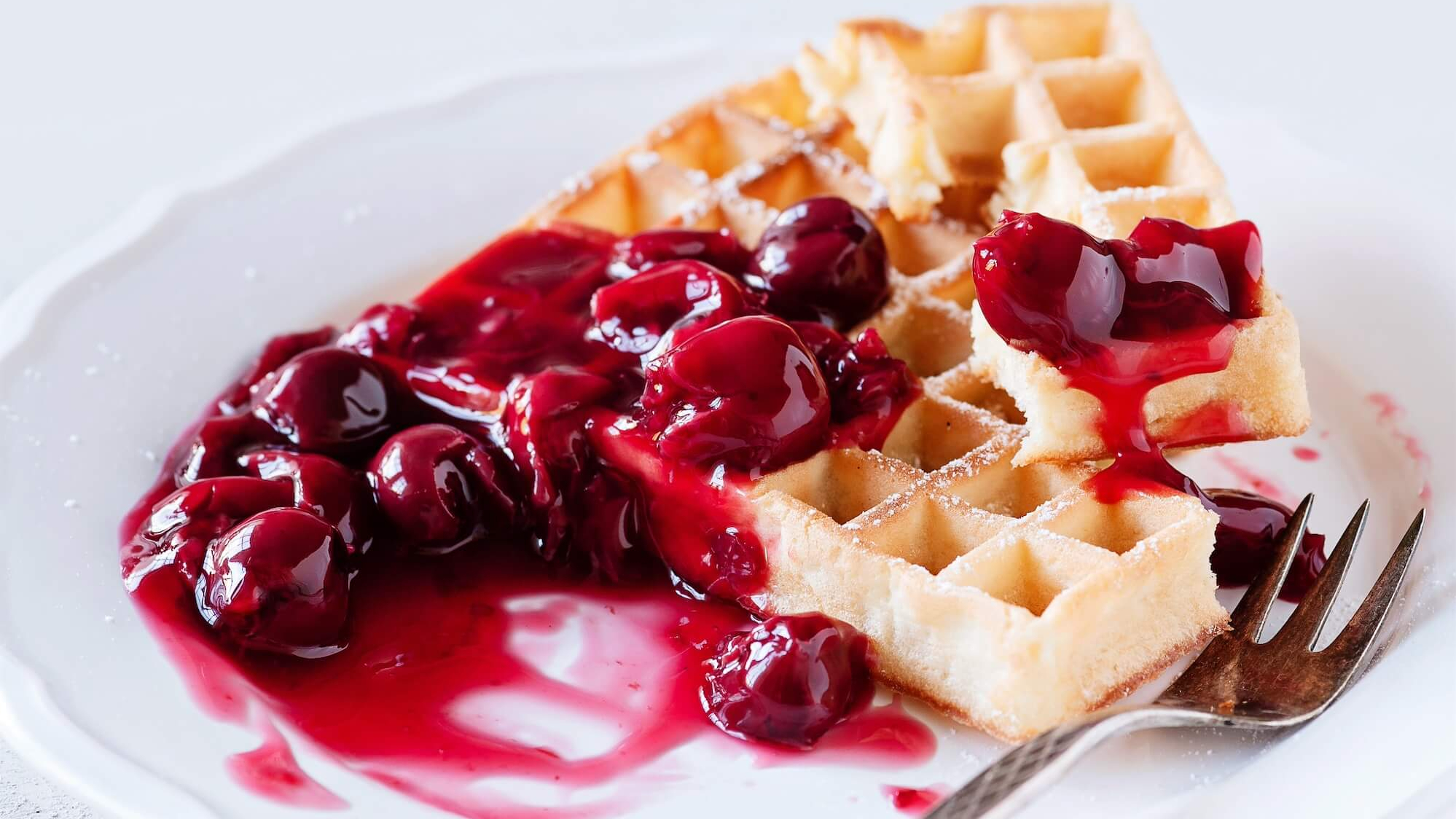 Eine Waffel mit Kirschen und Gabel auf einem Teller.