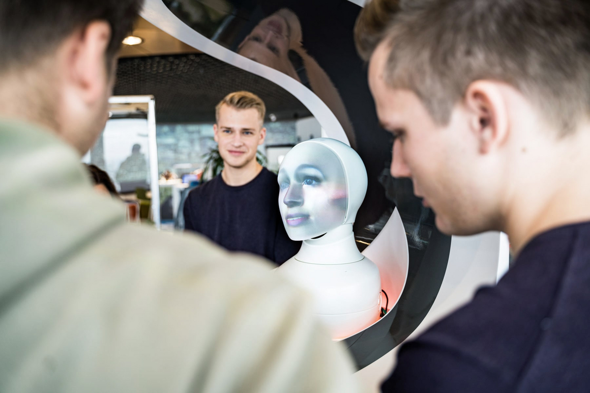 Zwei Männer stehen vor einem Spigel mit einem menschlich aussehenden Roboter.