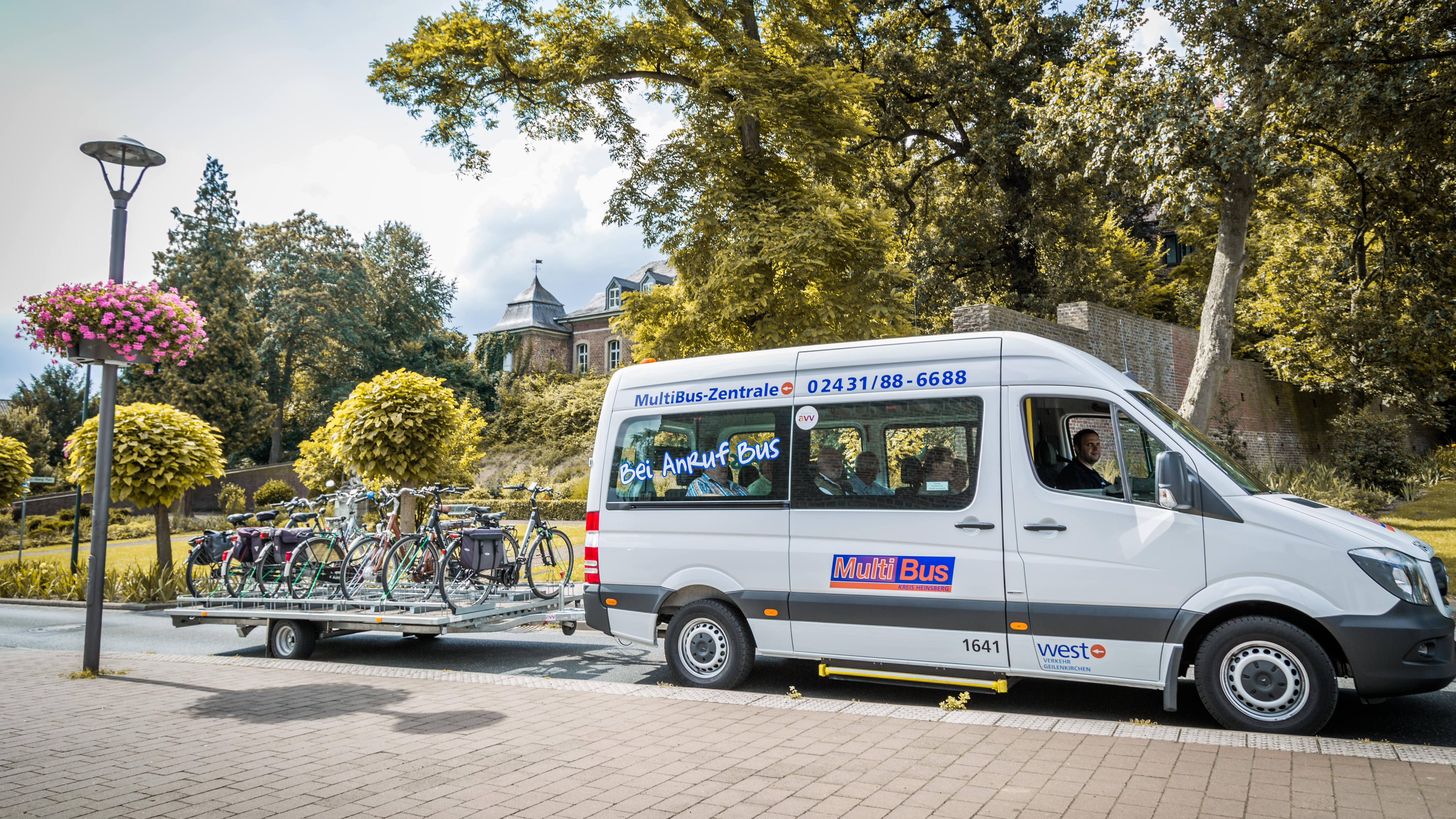 Ein Minibus steht auf einer grün bewachsenen Straße mit einem Fahrradanhänger.