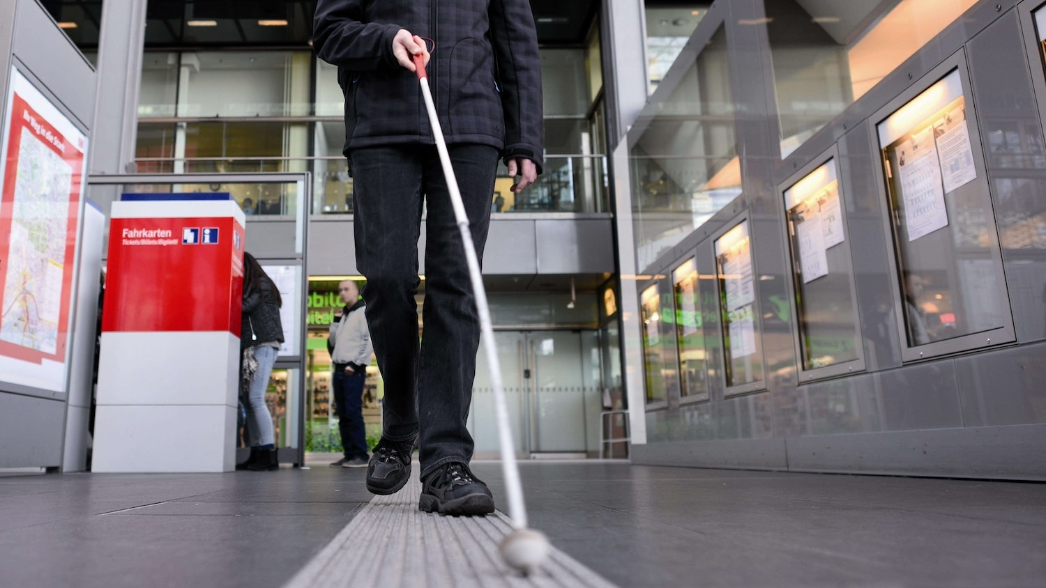 Mann mit Blindenstock im Bahnhof