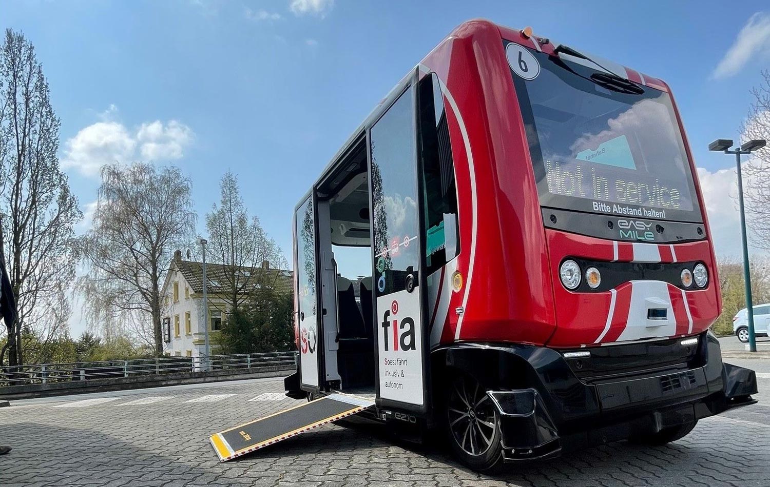 Ein kleiner rot-weißer Shuttlebus steht auf einem Platz und hat eine Rampe für Rollstuhlfahrer ausgeklappt.