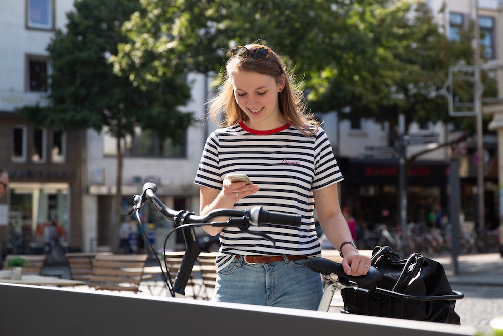 Eine junge Frau bucht über ihr Handy ein Leihrad.