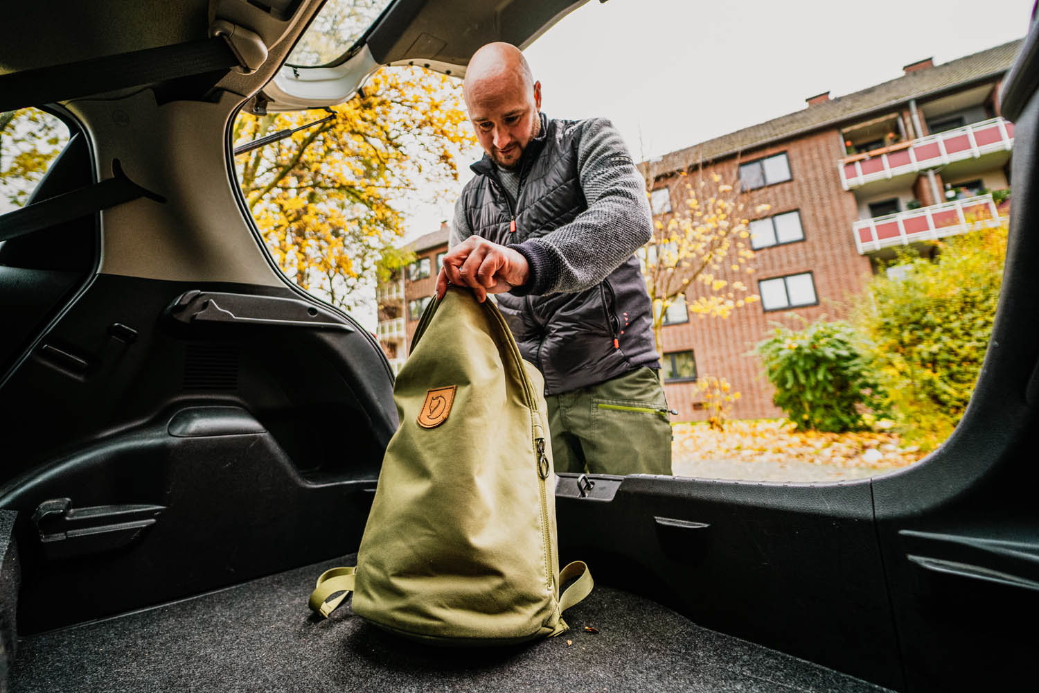 Ein Mann schaut in den Kofferraum eines Autos und stellt dort einen Rucksack ab.