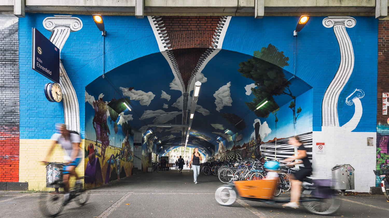 Der Bahnhof Köln-Ehrenfeld mit einem Kunstwerk in der Unterführung: Auf dem Gemälde wird durch einen Reißverschluss der blaue Himmel geschlossen.