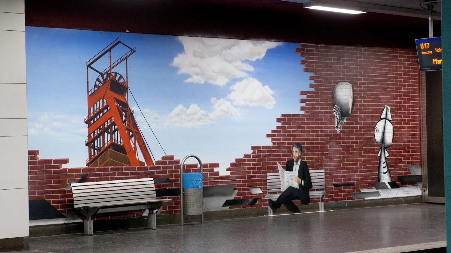 Ein Ruhrgebietsgemälde in Graffitiform an der U-Bahn Haltestelle Essen-Bismarckplatz: Man sieht den Förderturm der Zeche Zollverein vor einem blauen Himmel.