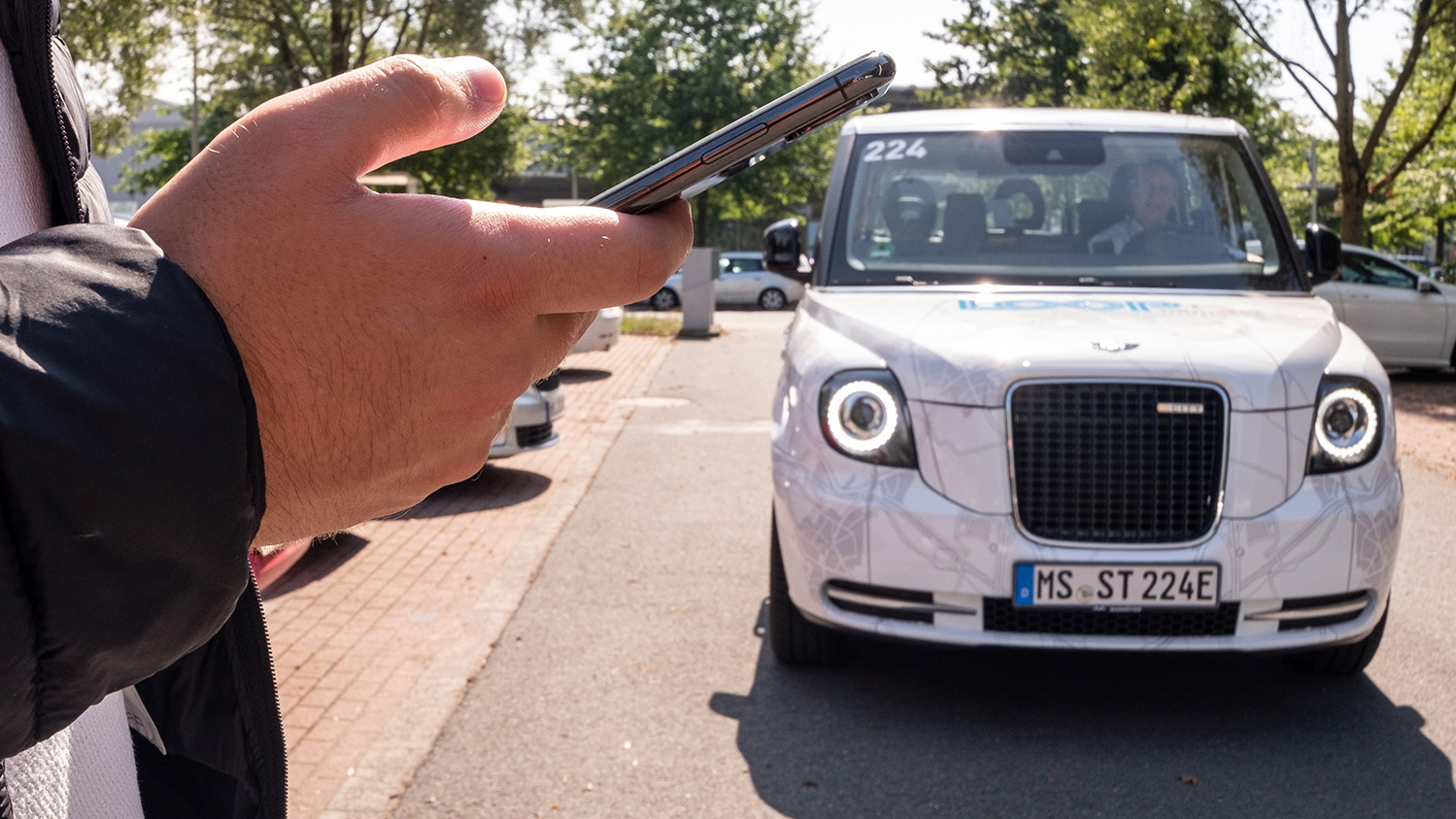 Ein Mann hält ein Handy in der Hand. Ein LOOPmünster-Fahrzeug komt auf ihn zu.