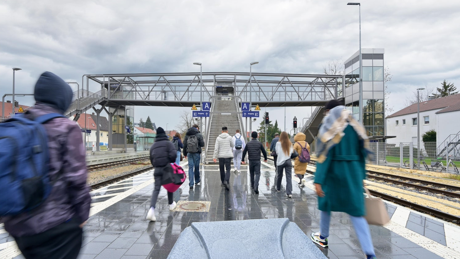 Menschen laufen über einen Bahnsteig, im Hintergrund ist eine Überführung