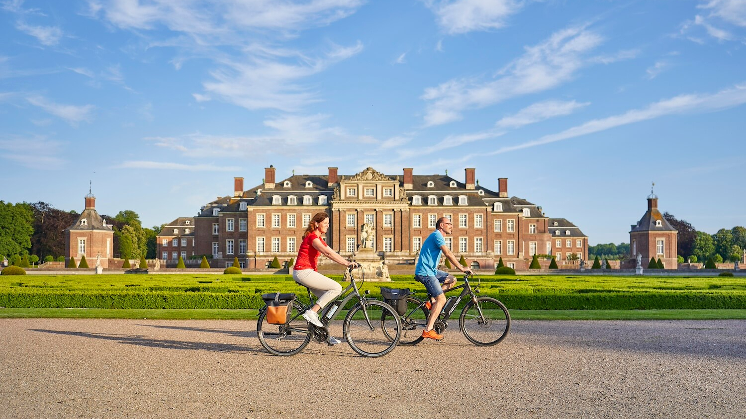 Zwei Personen auf E-Bikes radeln am Schloss Nordkirchen vorbei.