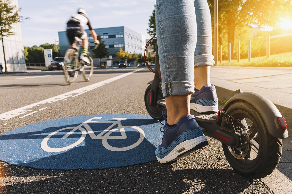 Eine Person fährt in einer Stadt auf der Fahrradspur mit einem E-Scooter.